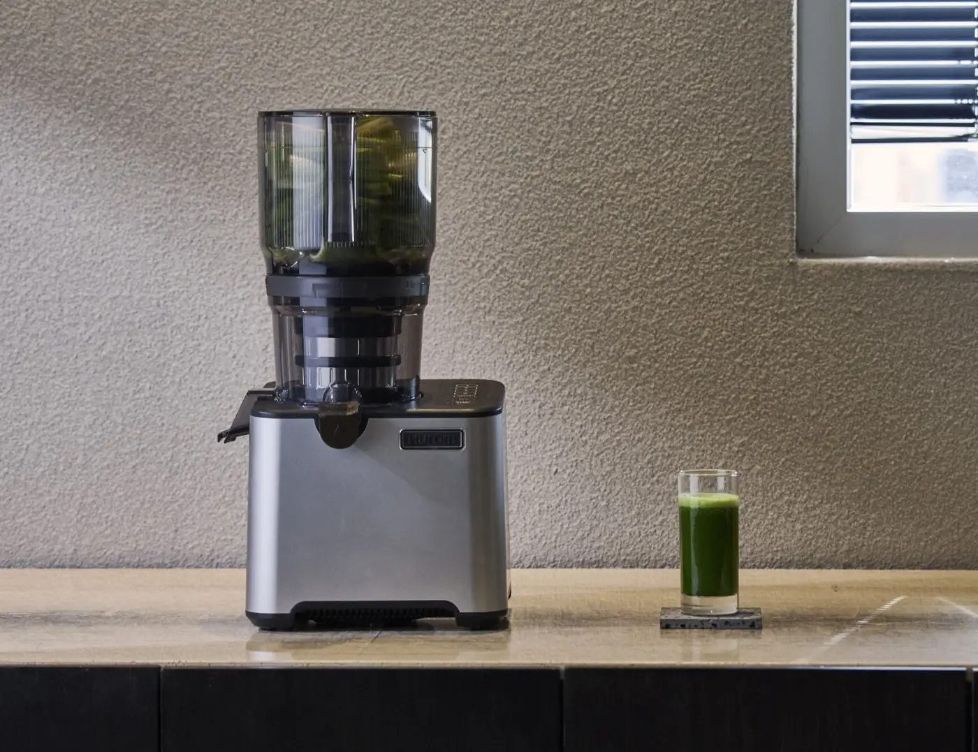 Hurom CP50 Commercial Slow Juicer in einer Küche neben einem Glas grünem Saft