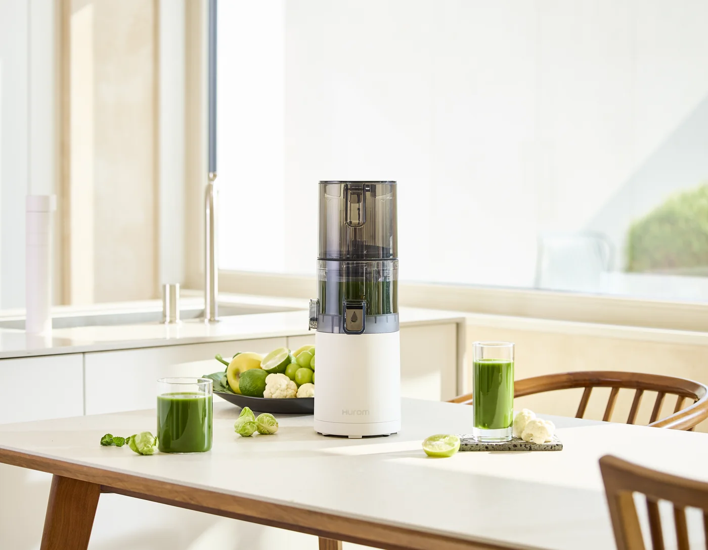 Hurom E30ST Slow Juicer auf einem Esstisch neben grünen Säften und frischen Zutaten