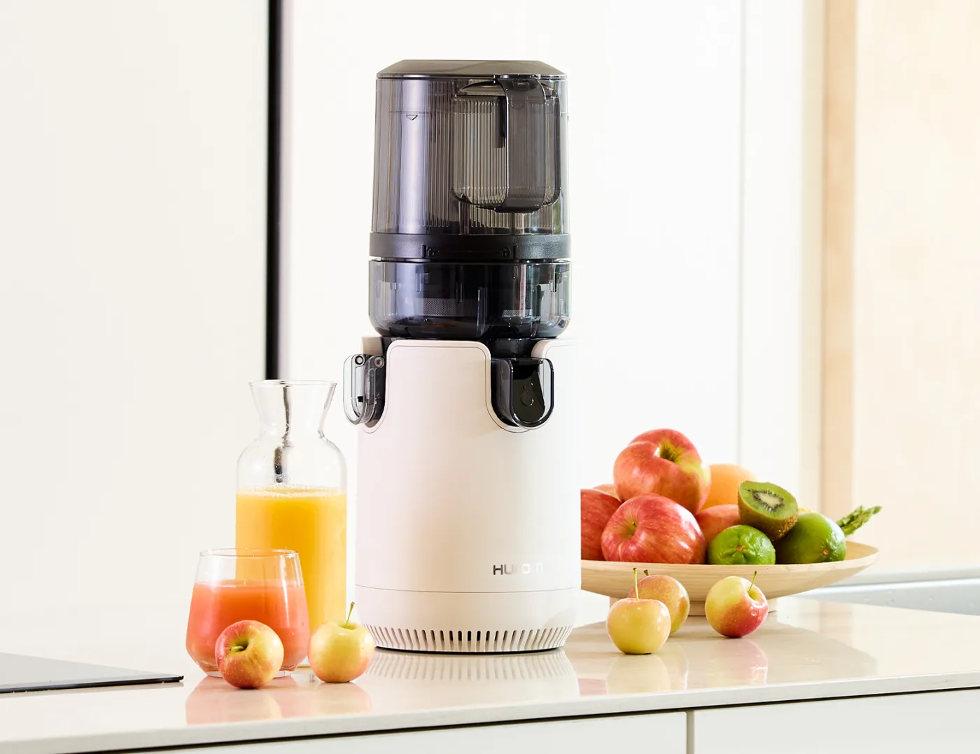 Hurom E50ST Slow Juicer auf einer Küchenarbeitsplatte neben frisch gepressten Säften und Äpfeln