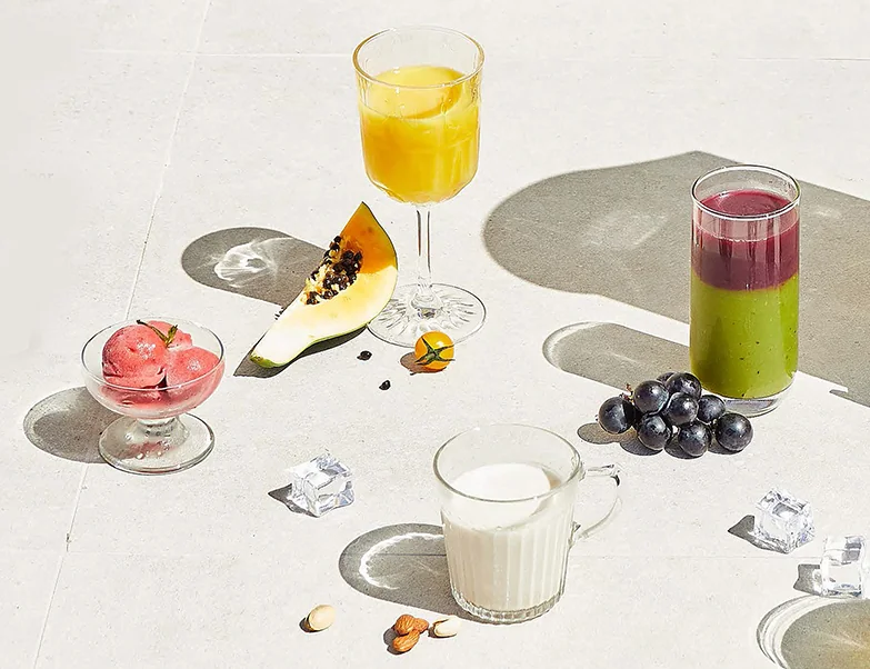 Frisch gepresste Säfte und ein Sorbet neben Obst auf einem hellen Tisch