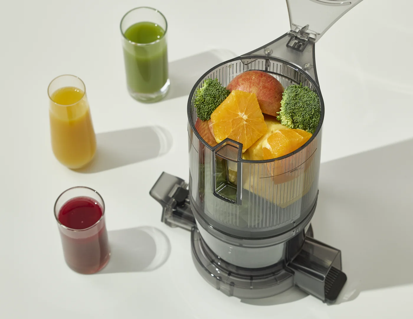 Einfüllkammer eines Hurom Slow Juicers gefüllt mit Orangen, Brokkoli und Apfel