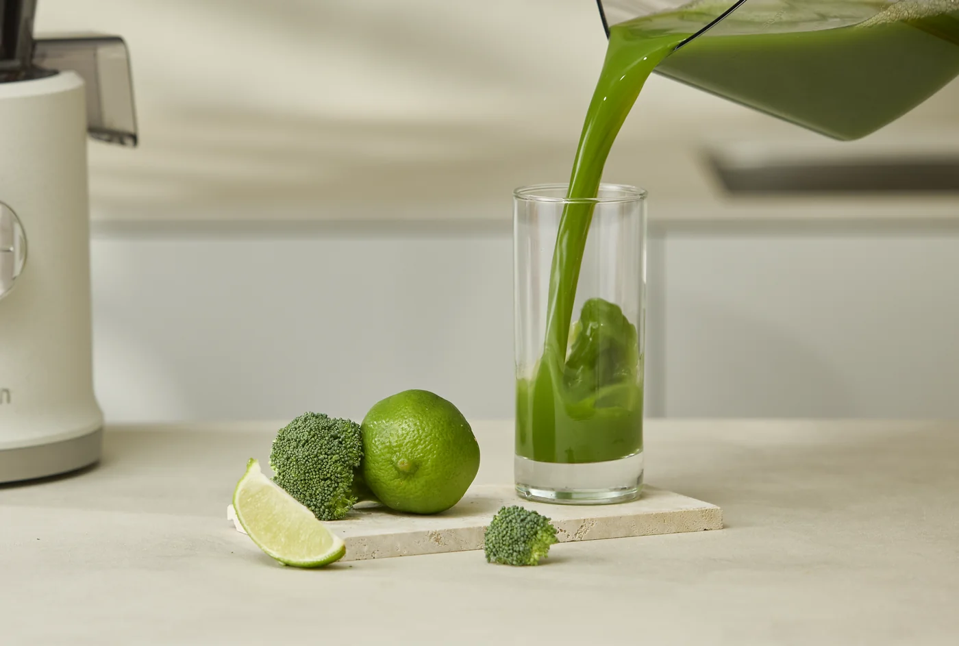 Grüner Saft wird frisch in ein Glas eingeschenkt, daneben Limette und Brokkoli